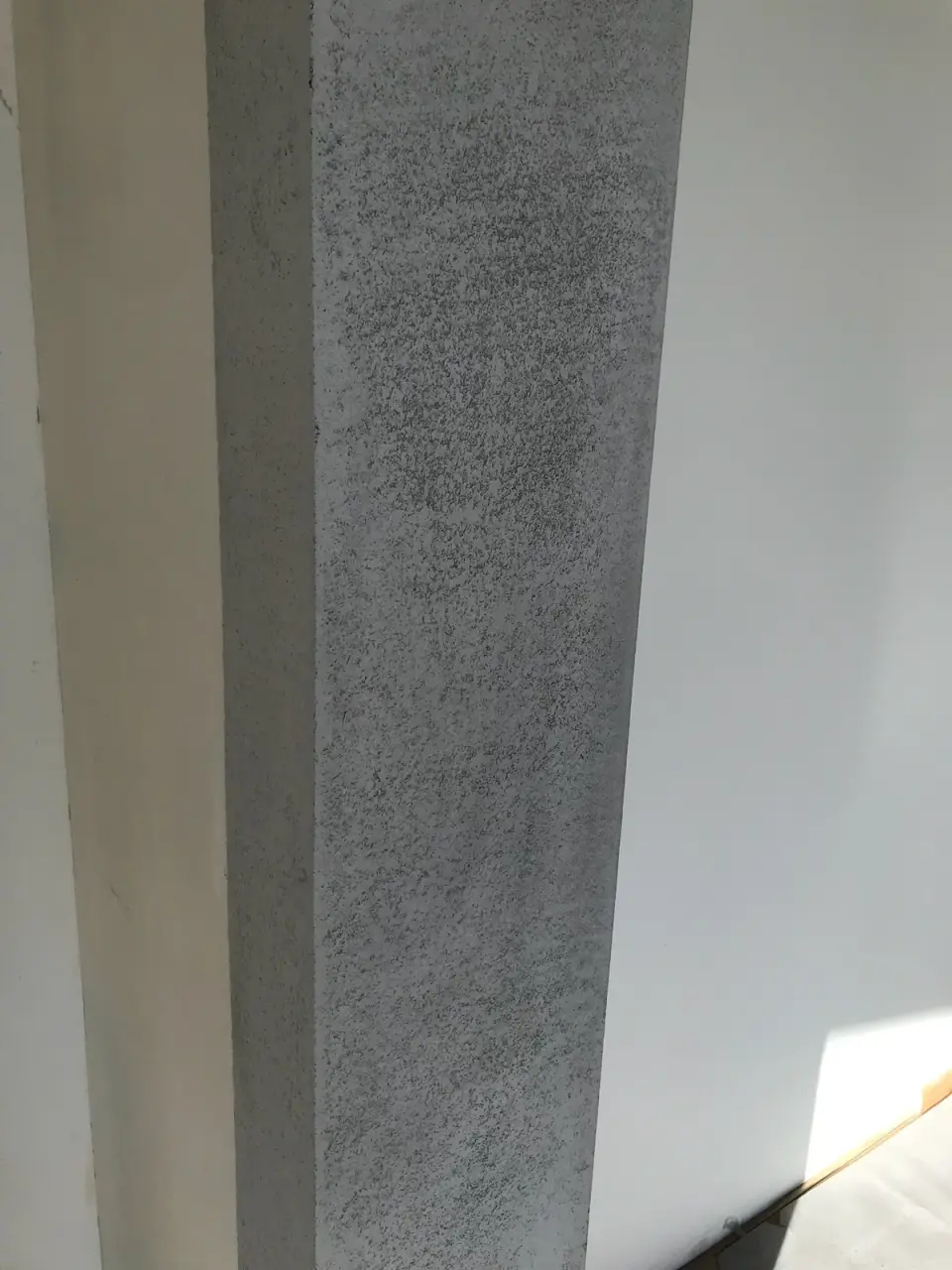 Sloup v šedé betonové stěrce vedle bílé stěny