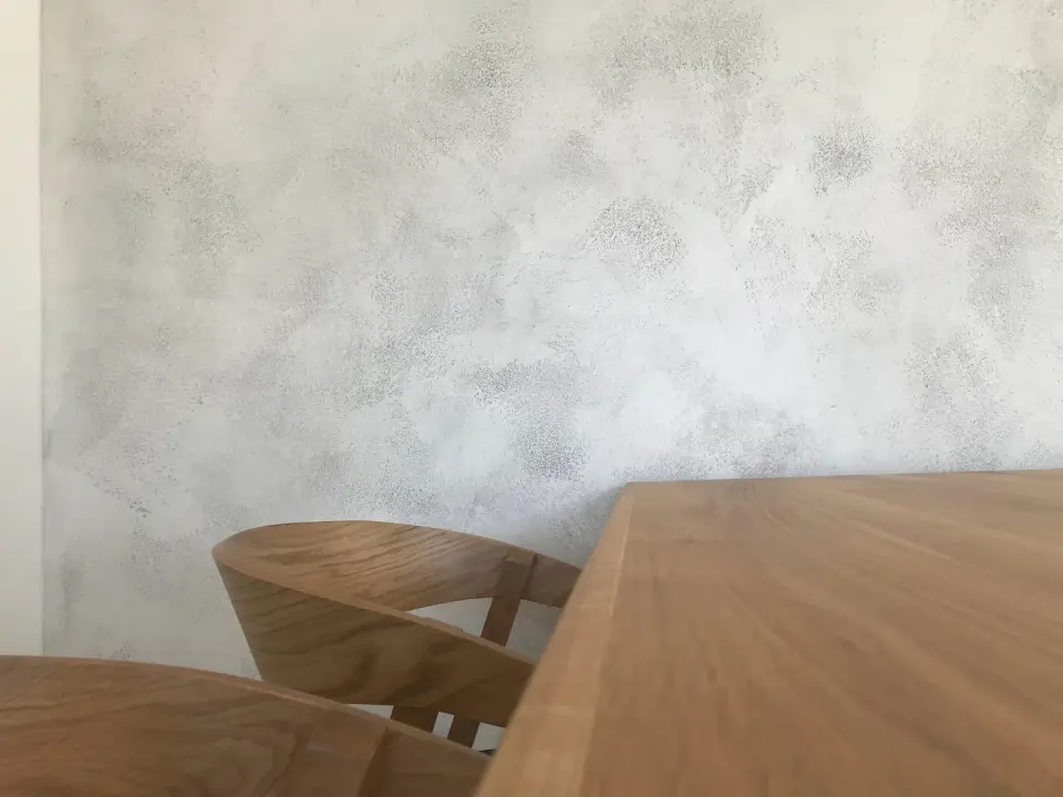 Jídelní kout s dubovým stolem a stěnou ve světlé betonové stěrce