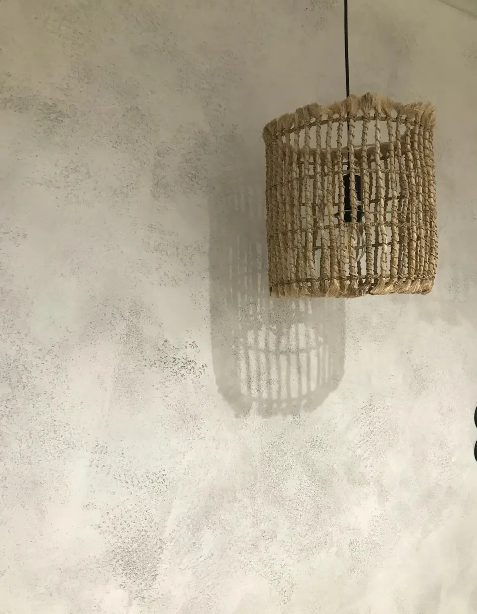 Ratanová lampa a její stín na světle šedé betonové stěrce