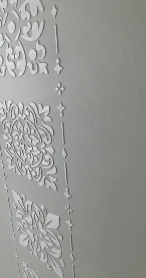Svislý pás bílých ornamentů na šedé stěrce stěny