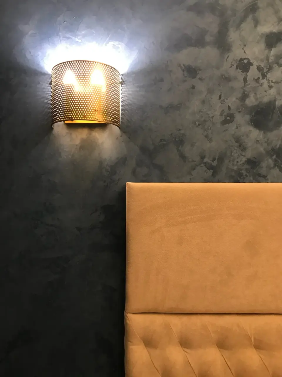 Detail modrošedé stěrky s nástěnnou lampou nad čelem postele