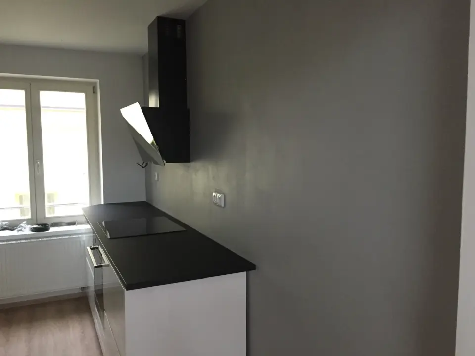 Kuchyňská linka s černou deskou a stěnou v hladké šedé stěrce