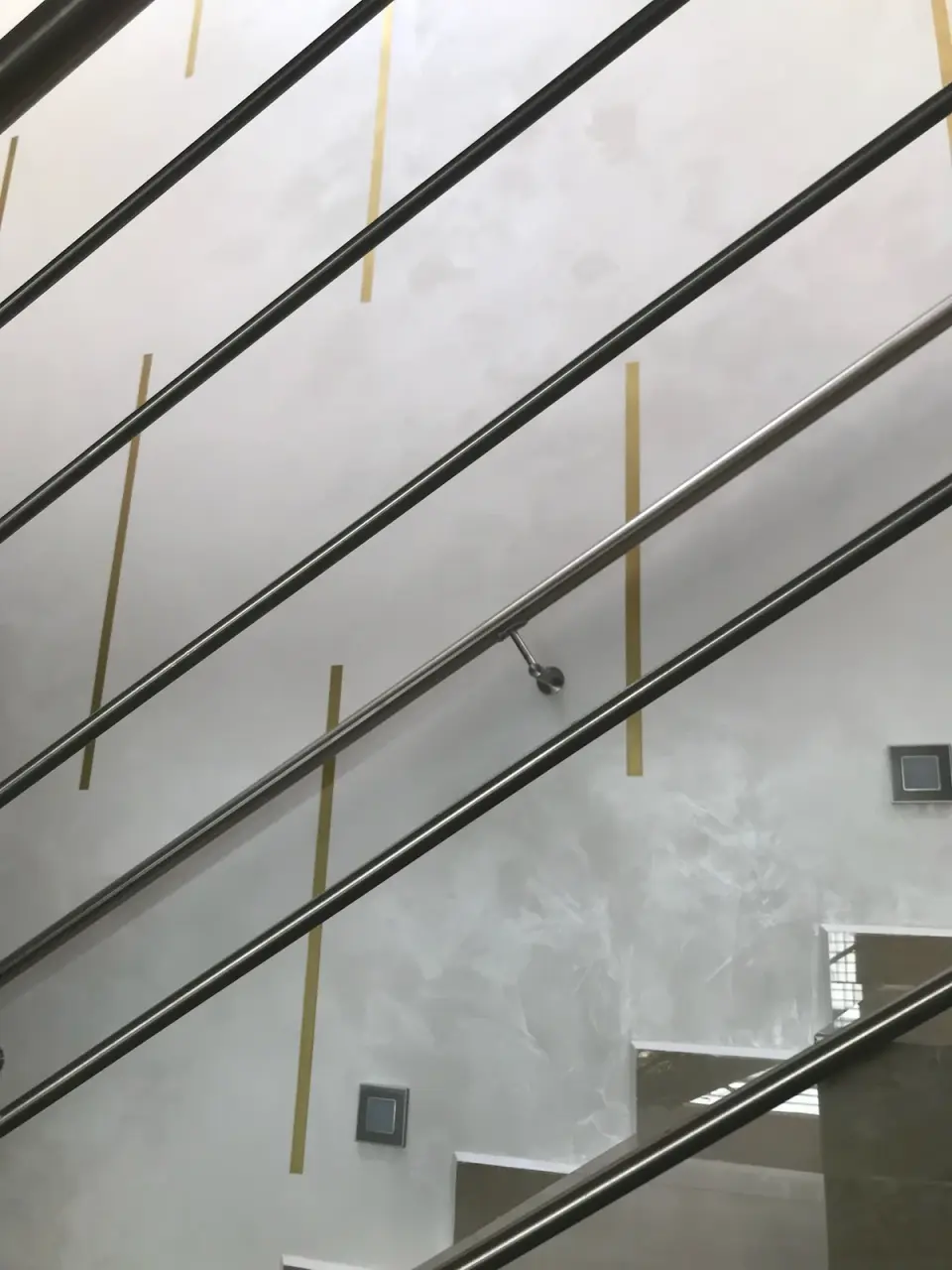 Mosazné pásky ve stěrce za nerezovým zábradlím schodiště