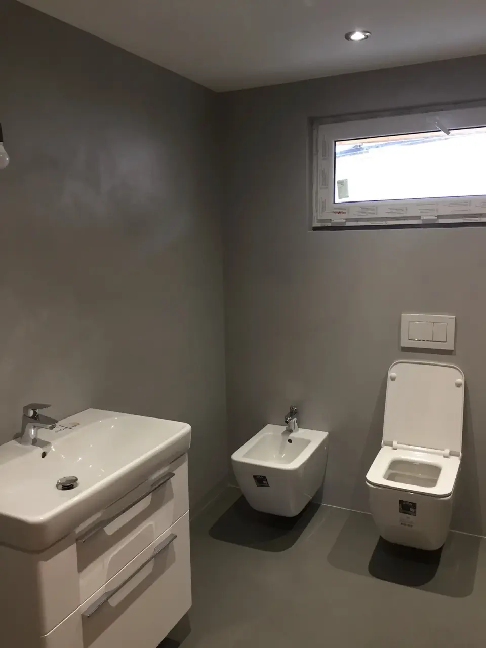 Šedá stěrka na stěnách a podlaze koupelny s WC a bidetem