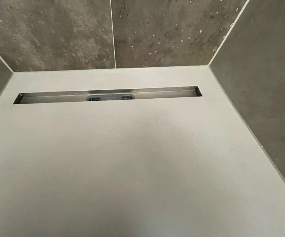 Podlaha sprchy ve světle šedé stěrce s nerezovým žlabem