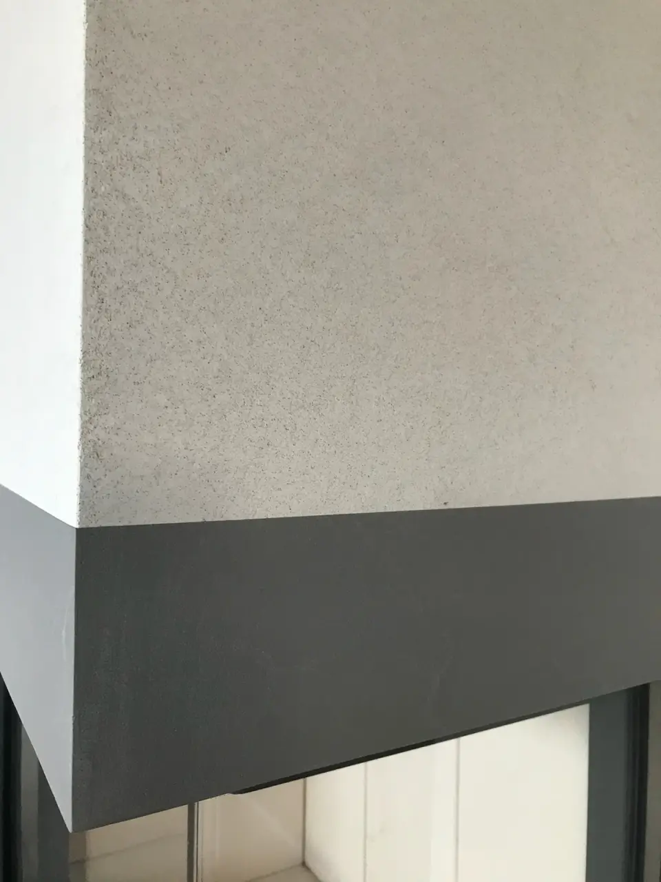 Detail jemně zrnité světlé stěrky nad tmavým rámem krbu