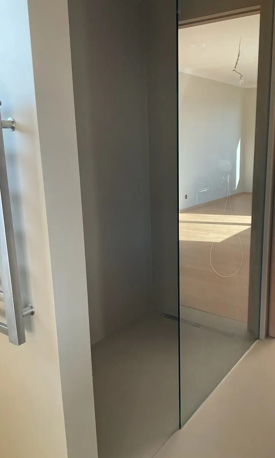 Sprcha za skleněnou stěnou se stěrkou na stěnách i podlaze