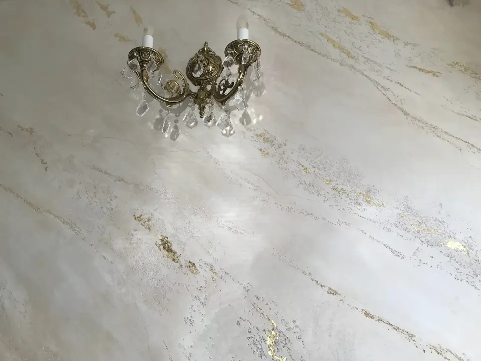 Mosazný svícen na světlé stěrce se zlatými a šedými žilkami