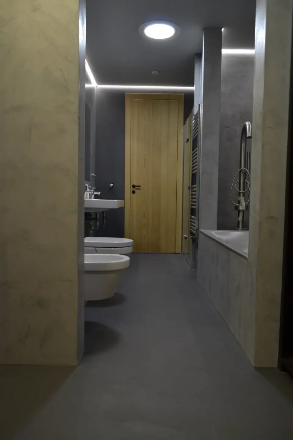 Pohled podél koupelny s vanou, WC a stěnami v šedé stěrce