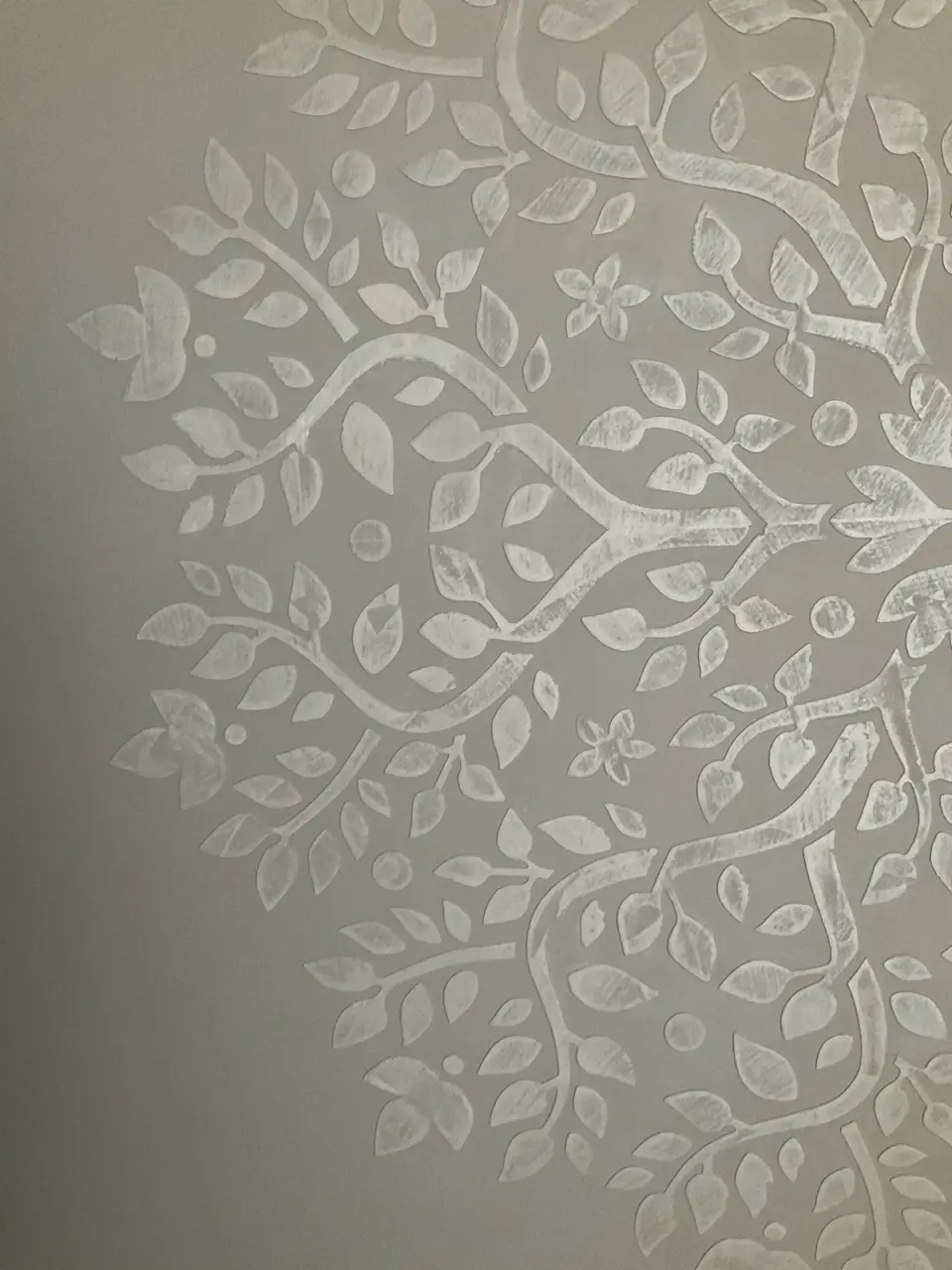 Detail bílého reliéfního ornamentu větví a listů na šedé stěrce