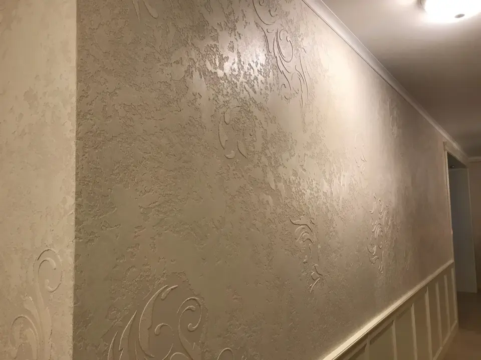 Dlouhá stěna chodby ve stěrce s ornamenty nad bílým obkladem