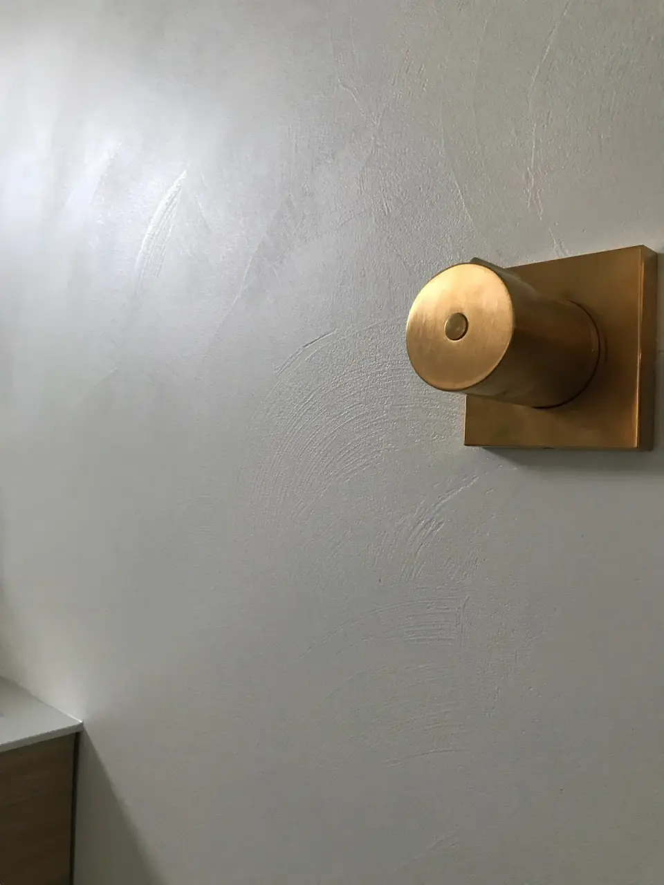 Zlatý držák sprchy na světlé stěrce se stopami hladítka