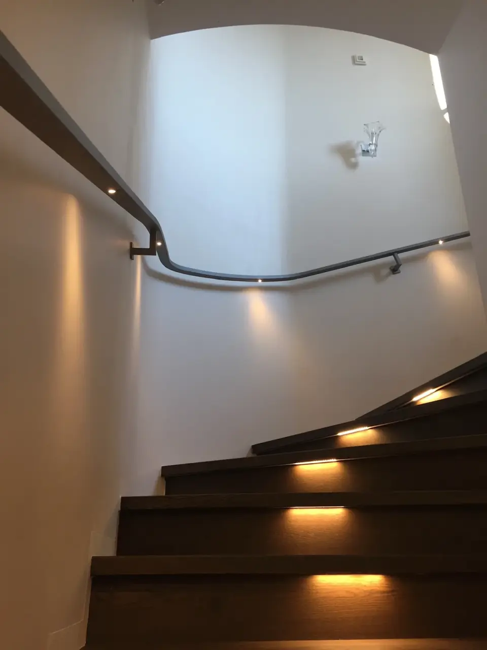 Zakřivená stěna schodiště ve světlé stěrce s madlem