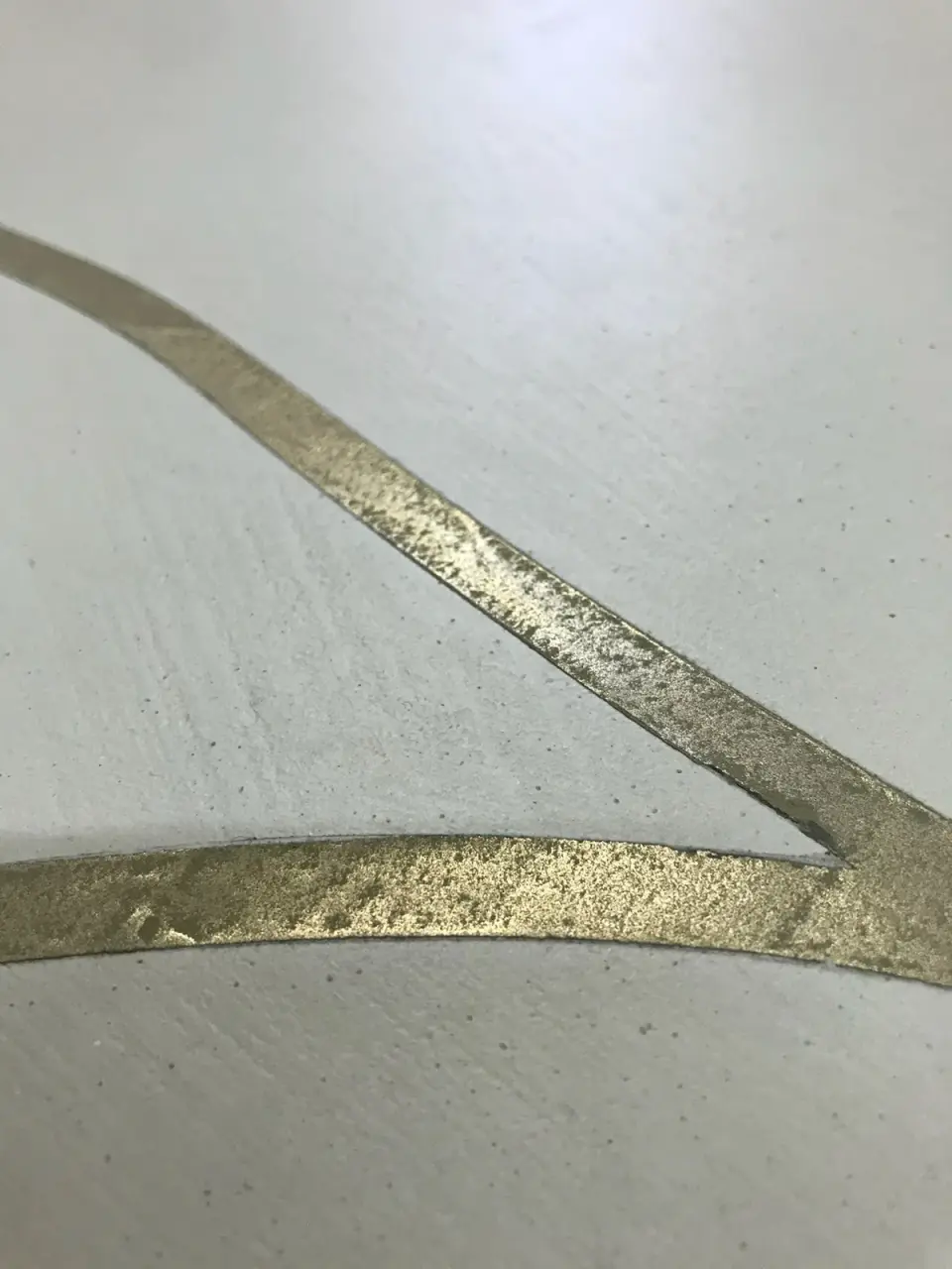 Detail zlatých kovových pásů zapuštěných do světlé stěrky