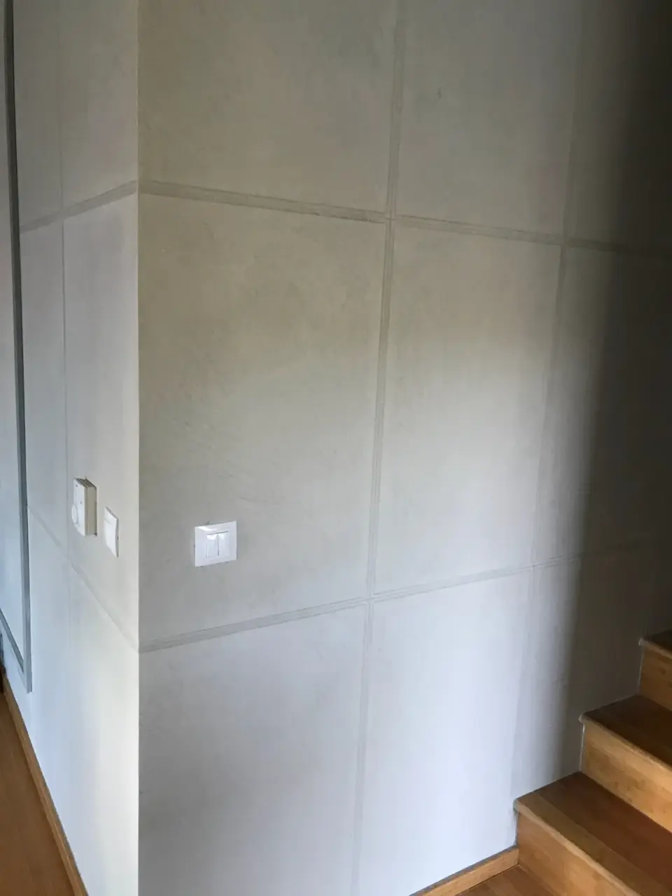 Stěna u schodiště ve světle šedé betonové stěrce s panely