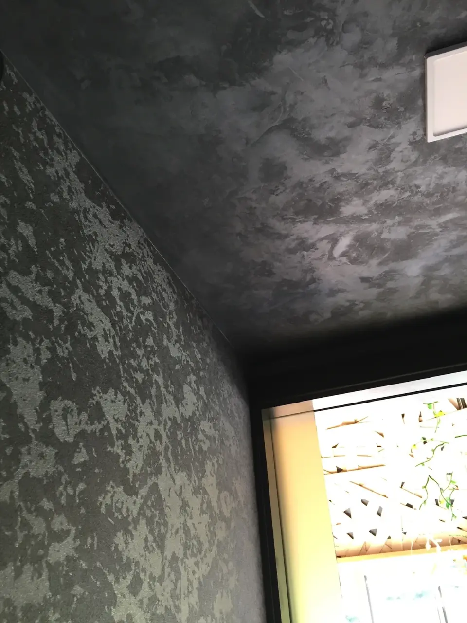 Kout s tmavým stropem a šedou skvrnitou stěrkou na stěně